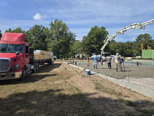 Crew working a large slab pour beside a flatbed truck and pump boom