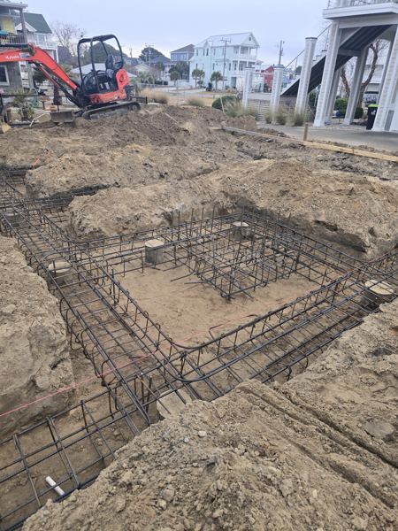 Rebar cages set in footing trenches beside raised coastal homes