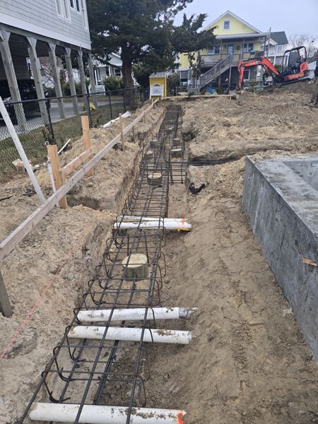 Rebar and pipe sleeves set in a footer trench next to a block wall