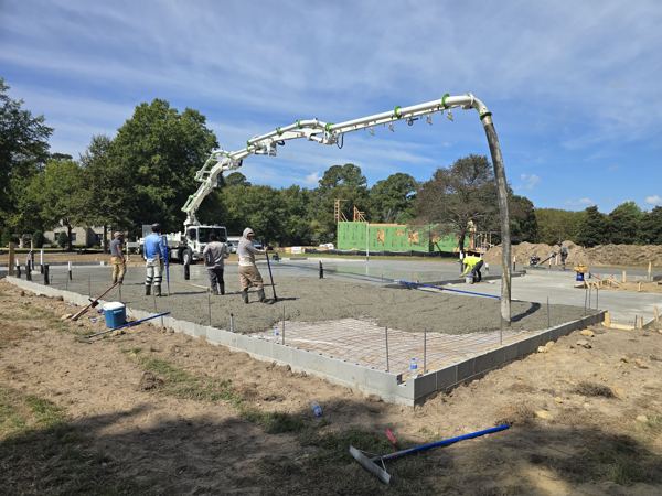 Pump boom placing concrete as a crew screeds a large slab